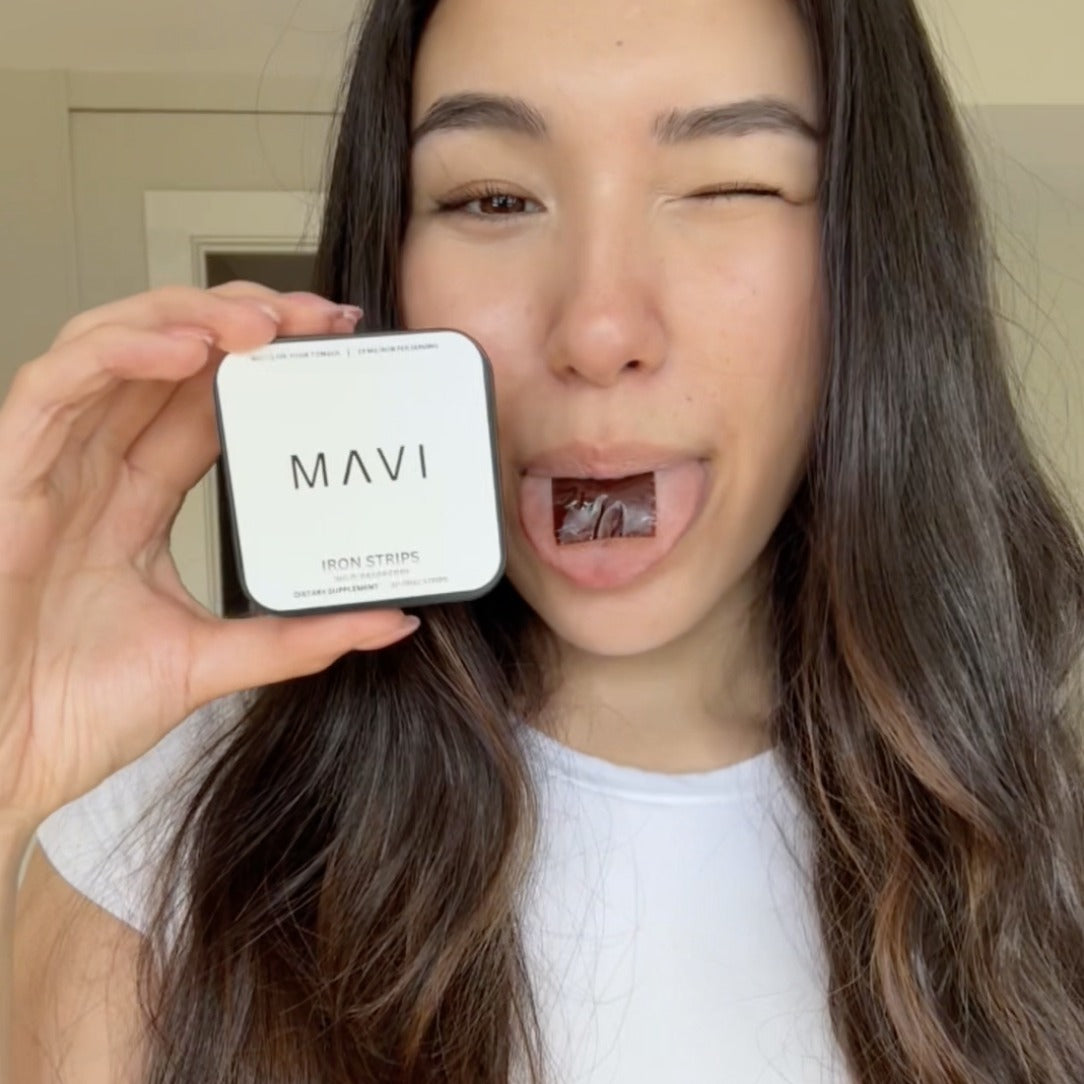 Woman holding a Mavi Iron Strips tin with a strip on her tongue